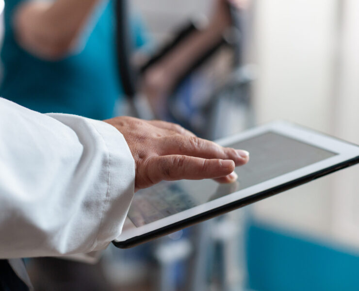 Close up of doctor using digital tablet with touch screen at physical recovery clinic. Medical worker holding modern device and technology to help patient with workout and fitness