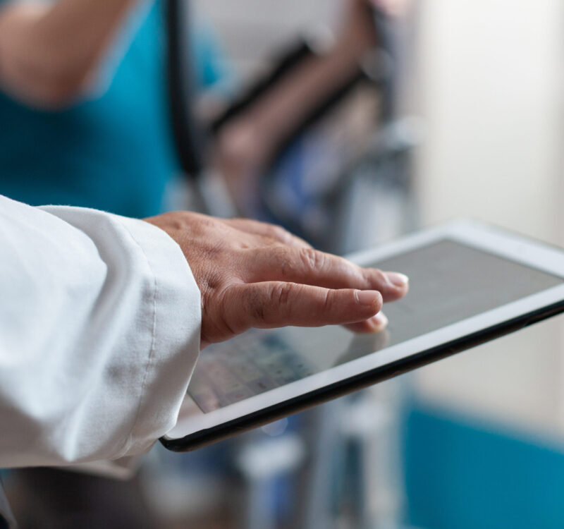 Close up of doctor using digital tablet with touch screen at physical recovery clinic. Medical worker holding modern device and technology to help patient with workout and fitness