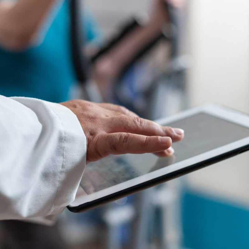Close up of doctor using digital tablet with touch screen at physical recovery clinic. Medical worker holding modern device and technology to help patient with workout and fitness